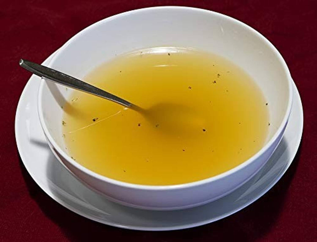 White bowl of golden broth with spoon on a plate
