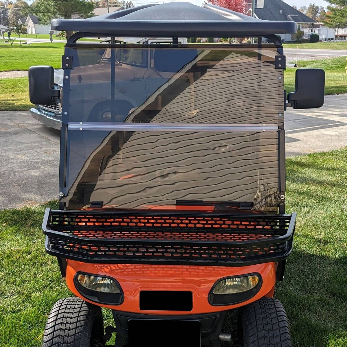 Front view of tinted fold-down windshield on golf cart, smoke glass panel in black frame.