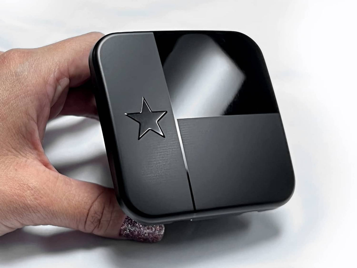 Black metal hitch cover plug with Texas star emblem, shown in hand near receiver.