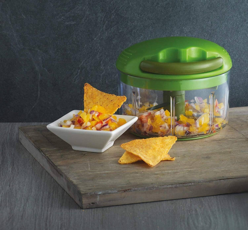 Green pull-cord food chopper with clear bowl near a white dish of chopped vegetables