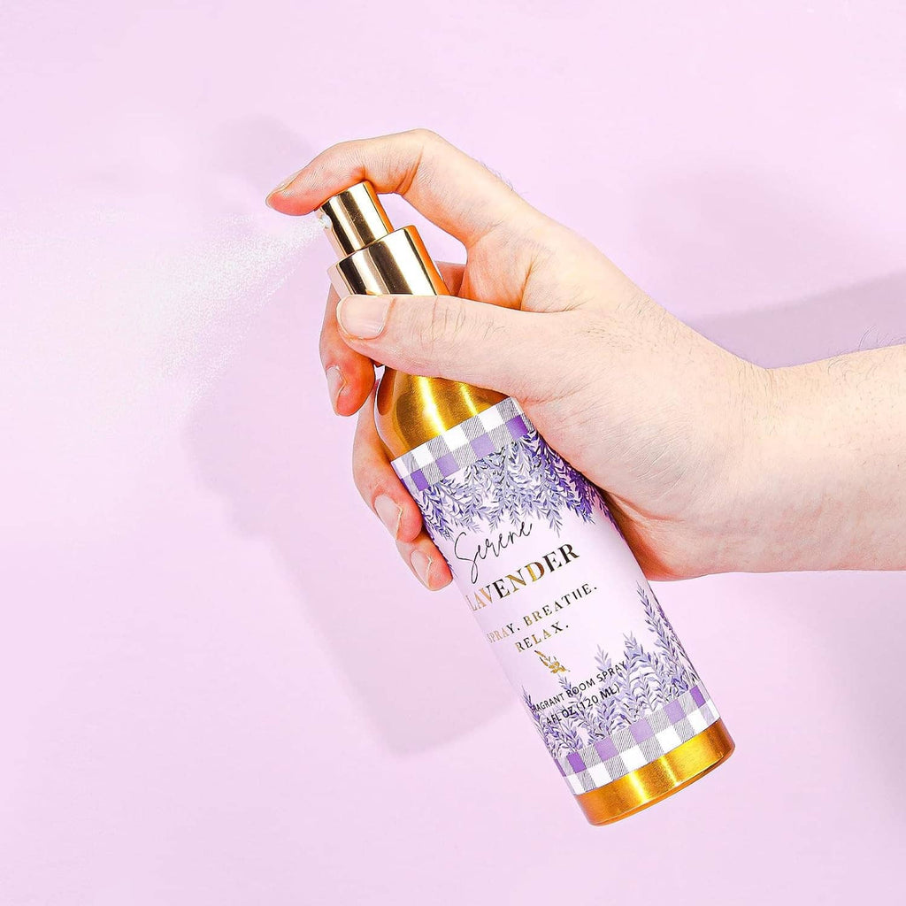 Hand holding a lavender room spray bottle with gold cap over a light background