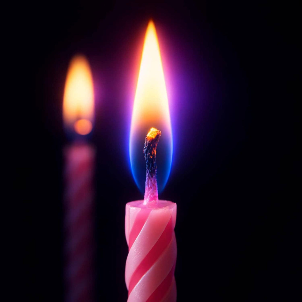 Lit pink spiral birthday candle with flame, blue and white candles in view