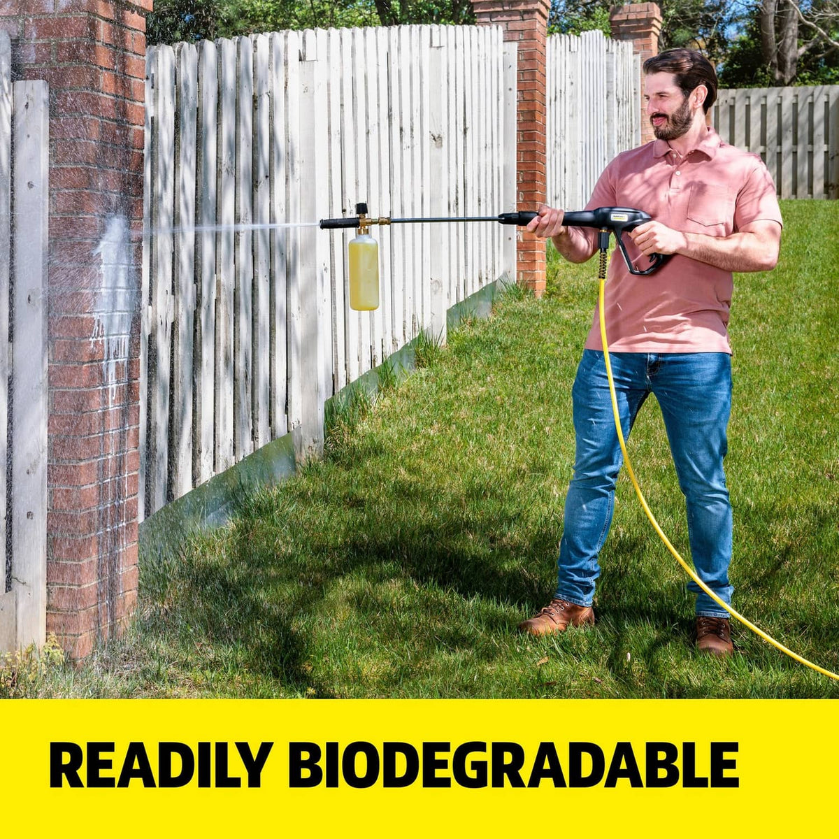 House and siding cleaner use: person pressure-washing a fence with a hose and wand