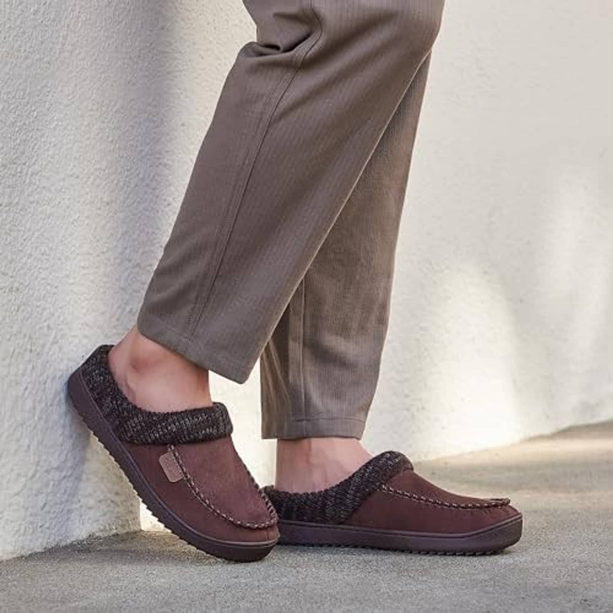 Brown moccasin clog slippers with dark knit cuffs worn with gray pants