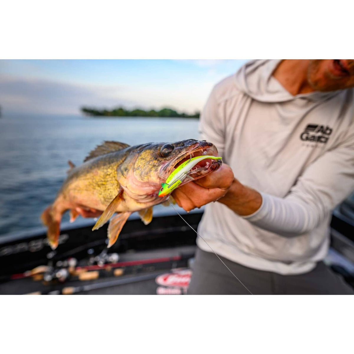 Soft fishing lure in fish mouth, green-and-orange body with hook and tail visible