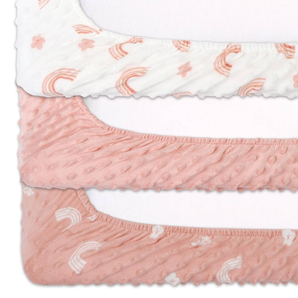 Stacked minky changing pad covers in white and pink with rainbow and flower patterns