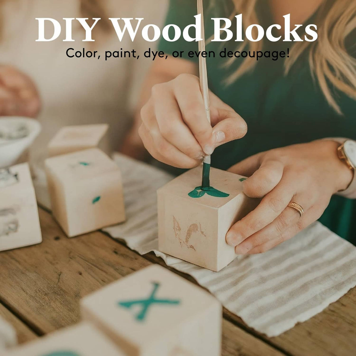 Small blank wooden cubes being painted by hands, with a cube held for customization