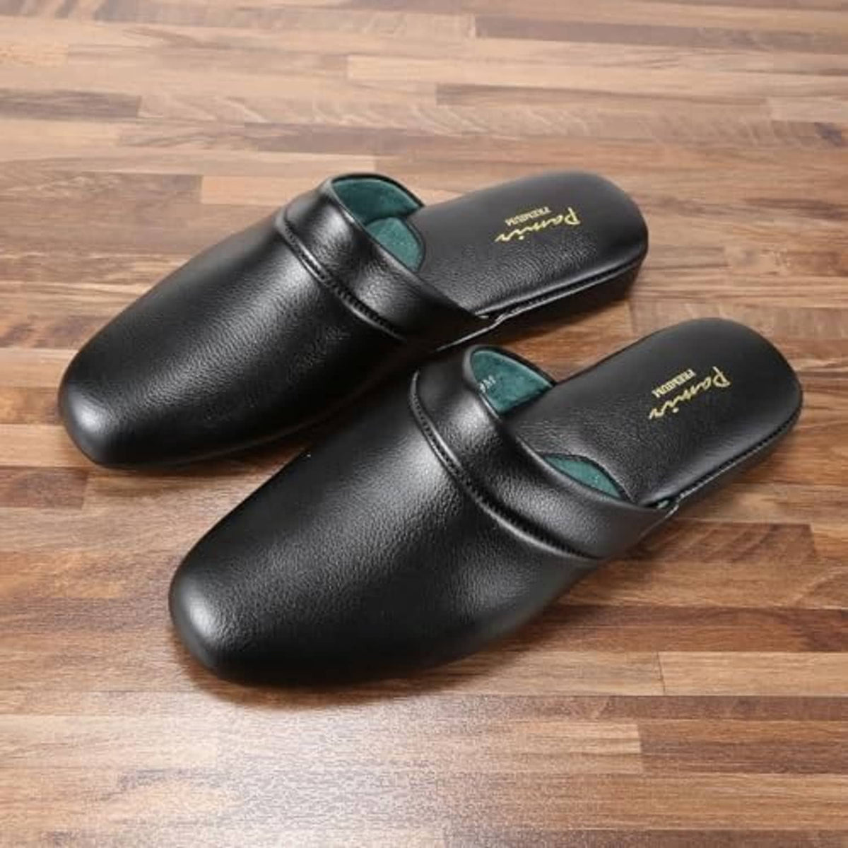 Black leather scuff slippers with teal lining, slip-on pair on wooden floor