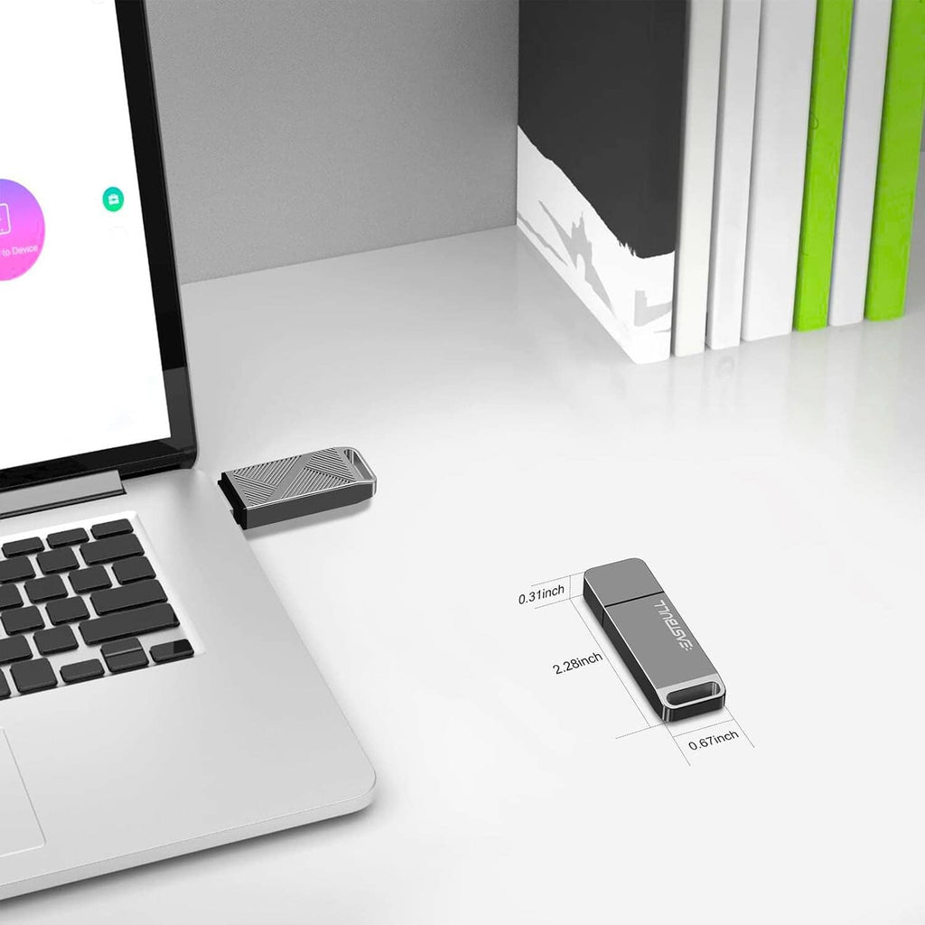 Grey USB flash drive with keychain size comparison on desk beside laptop