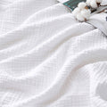 White 4-layer cotton muslin blanket, textured weave close-up with folded edge