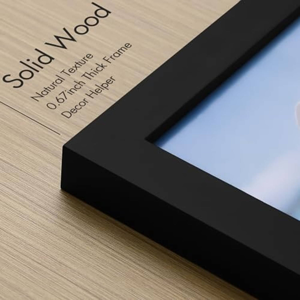 Close-up of black picture-frame corner over light wood, with clear plexiglass edge.
