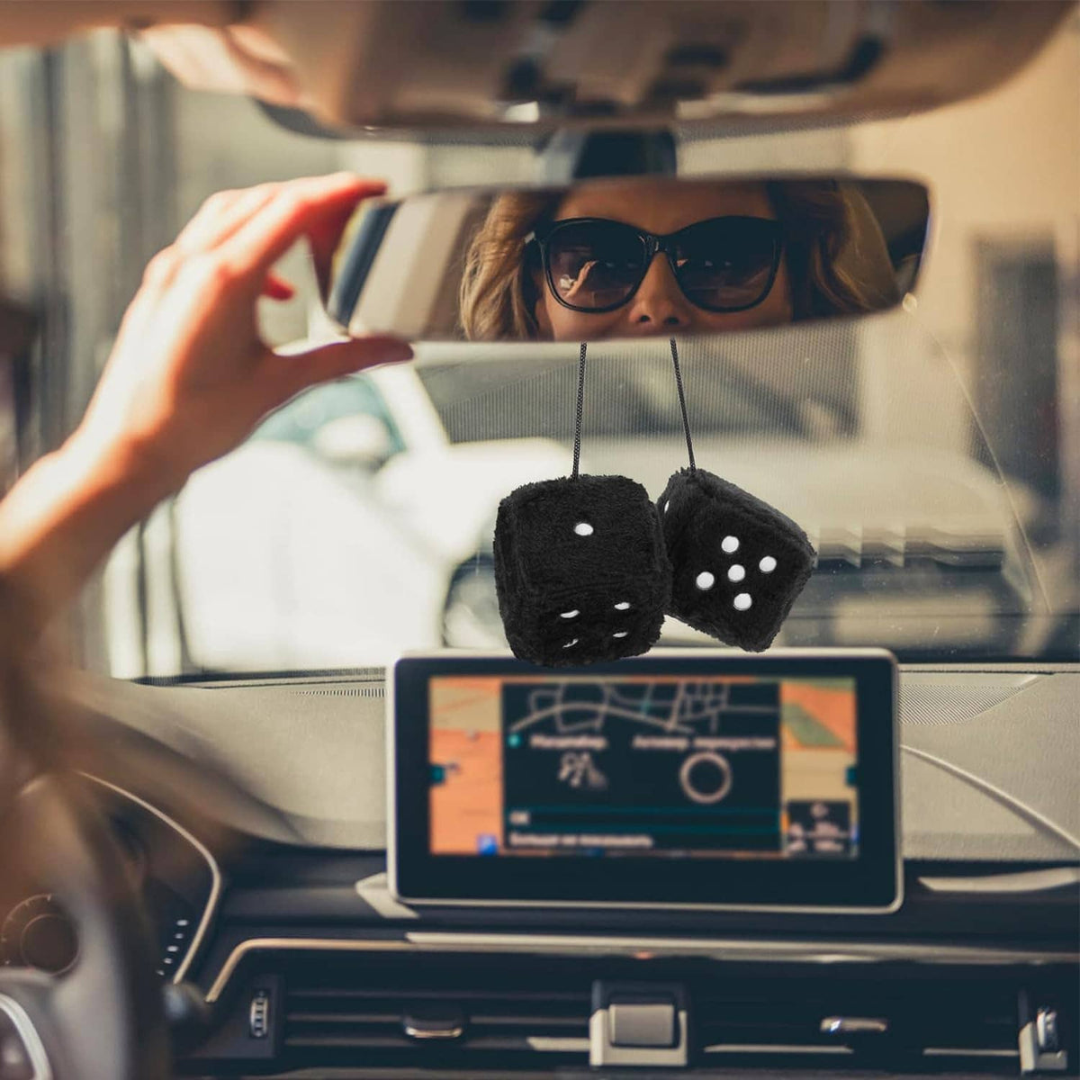 Pair of black fuzzy dice with white dots hanging from rear-view mirror inside car