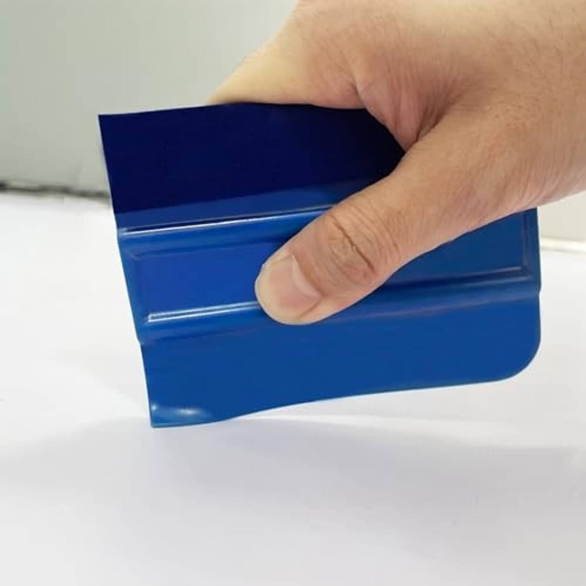Hand using blue felt vinyl squeegee tool with ribbed release edge