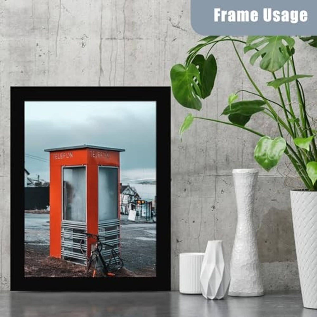 Black photo frame with glass front standing on floor against concrete wall