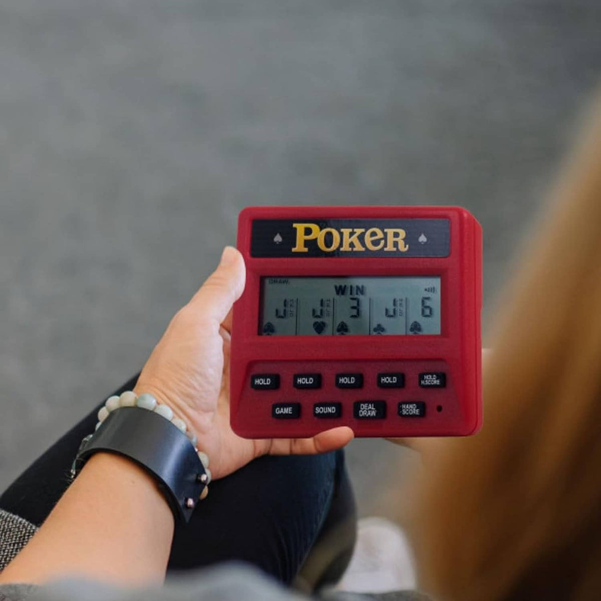 Red pocket poker game in hand with LCD screen and hold buttons visible.