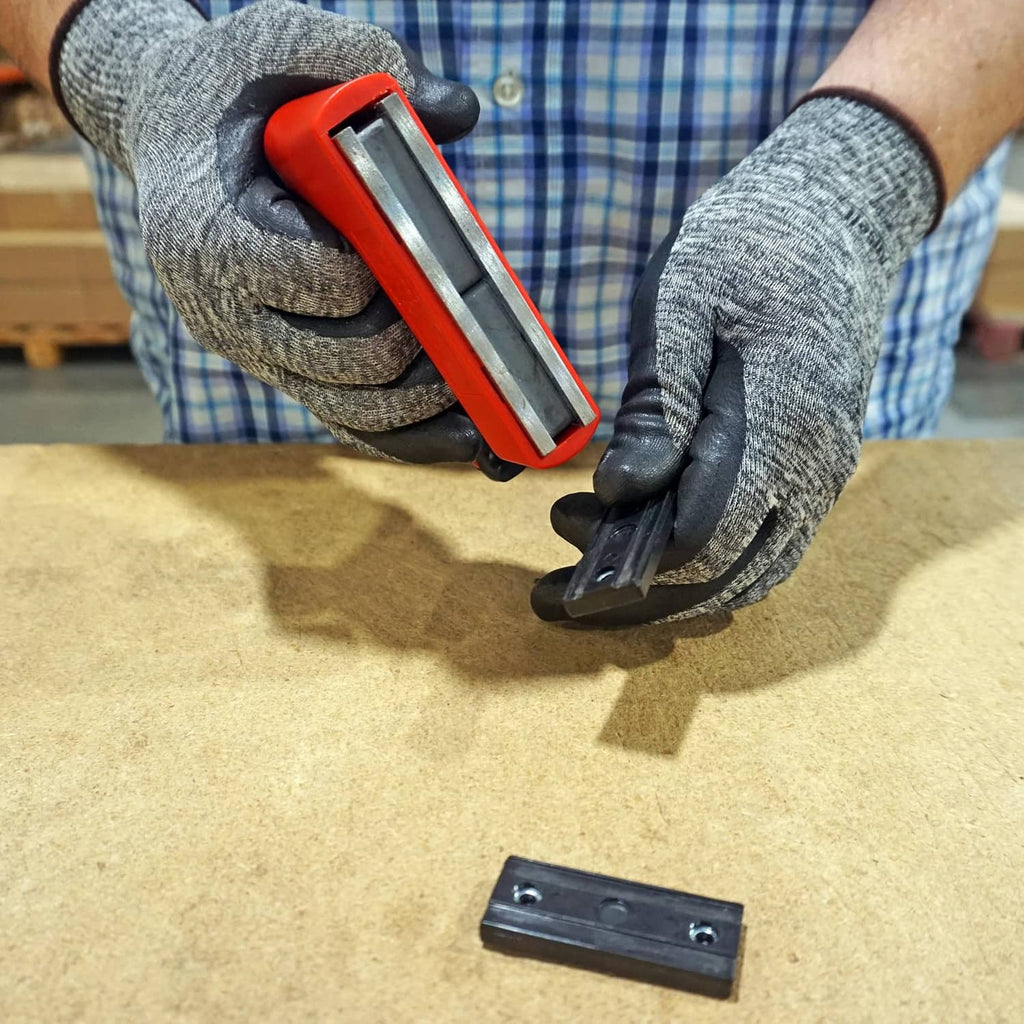Orange handle pull magnet held by gloved hands beside dark steel plate