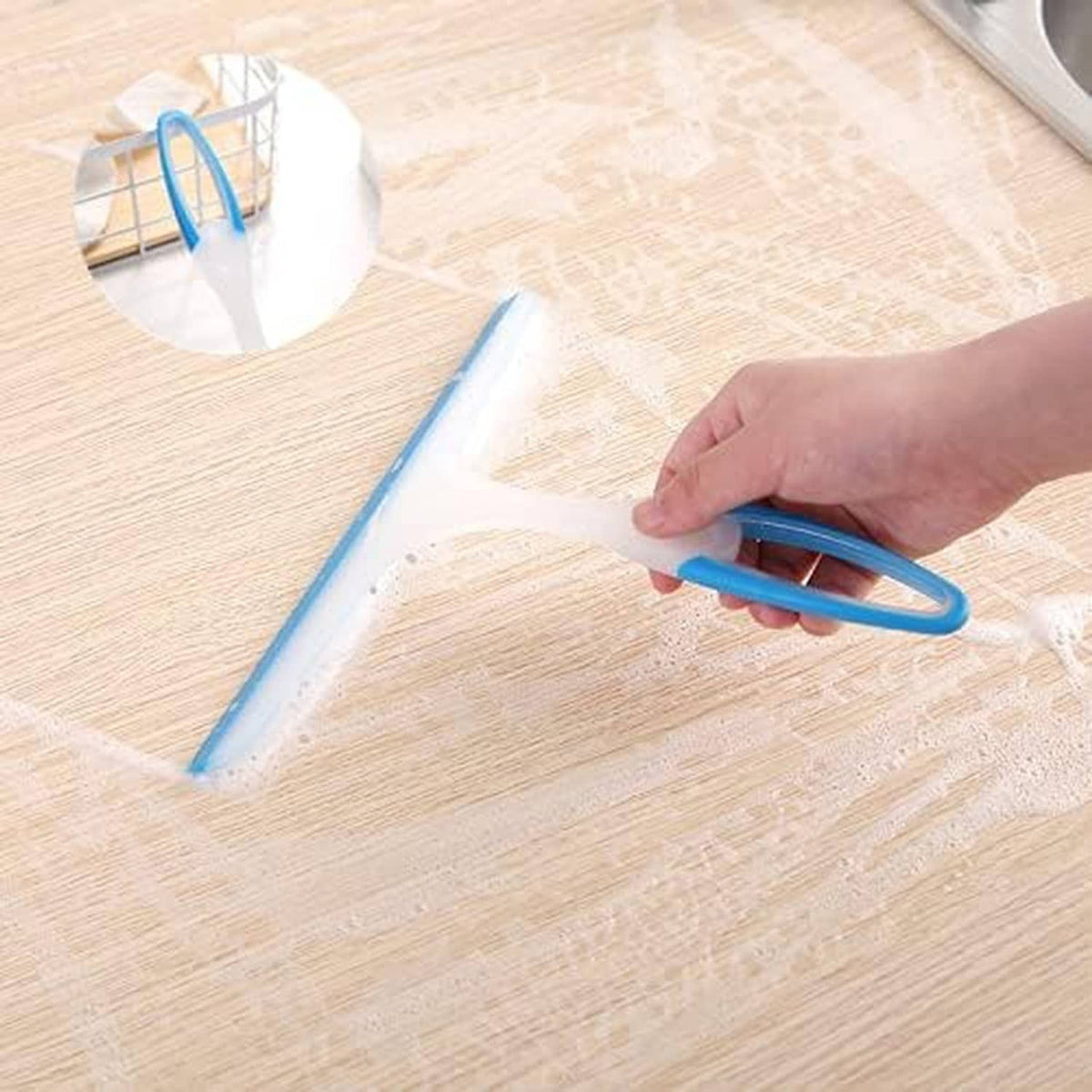 Hand using a blue silicone squeegee with white handle to remove water from a floor.