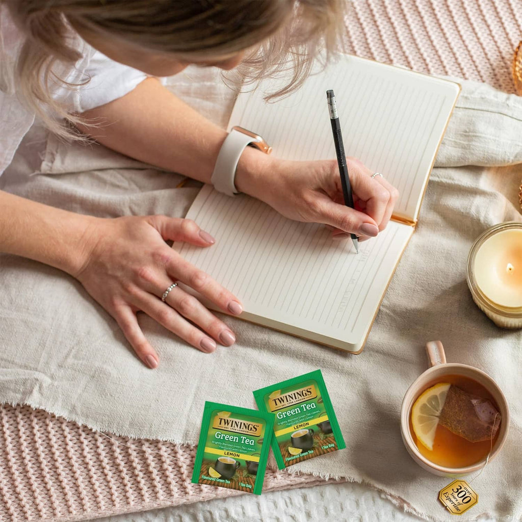 Green tea lemon tea bags in foil packets beside cup and notebook scene