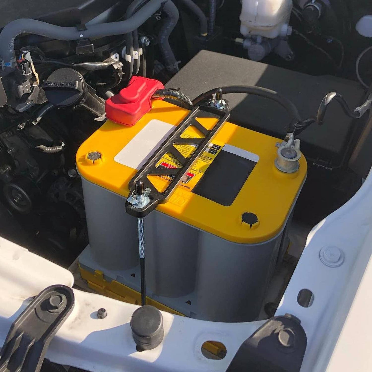 Battery hold-down bracket with two J-hooks and nuts mounted on a car battery top