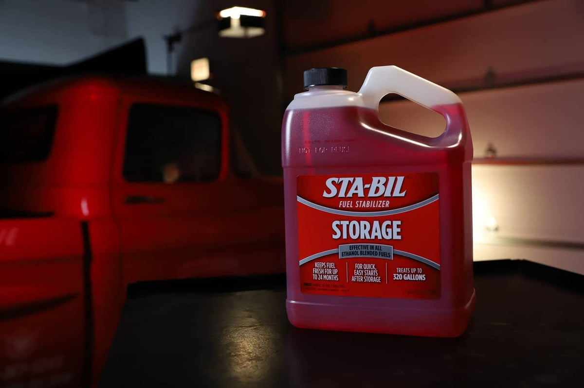 Red fuel stabilizer jug near a red vehicle inside a garage setting