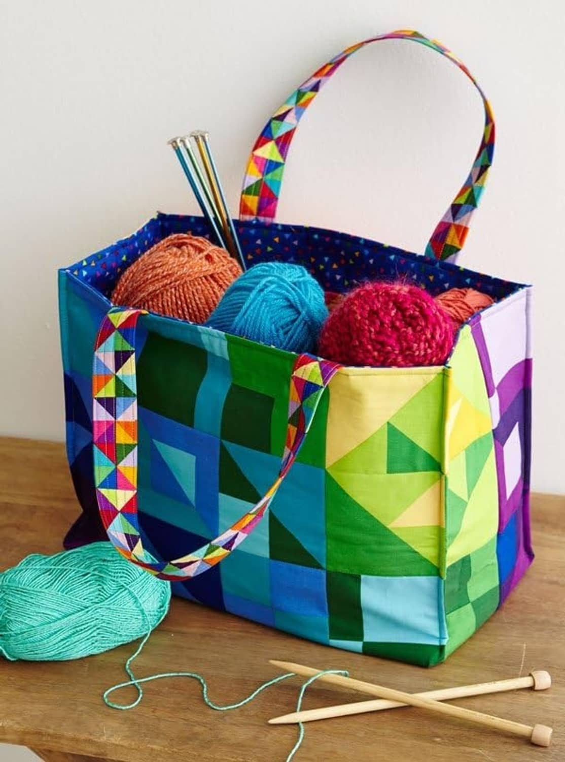 Patchwork fabric tote bag holding colorful yarn balls with crafting tools nearby