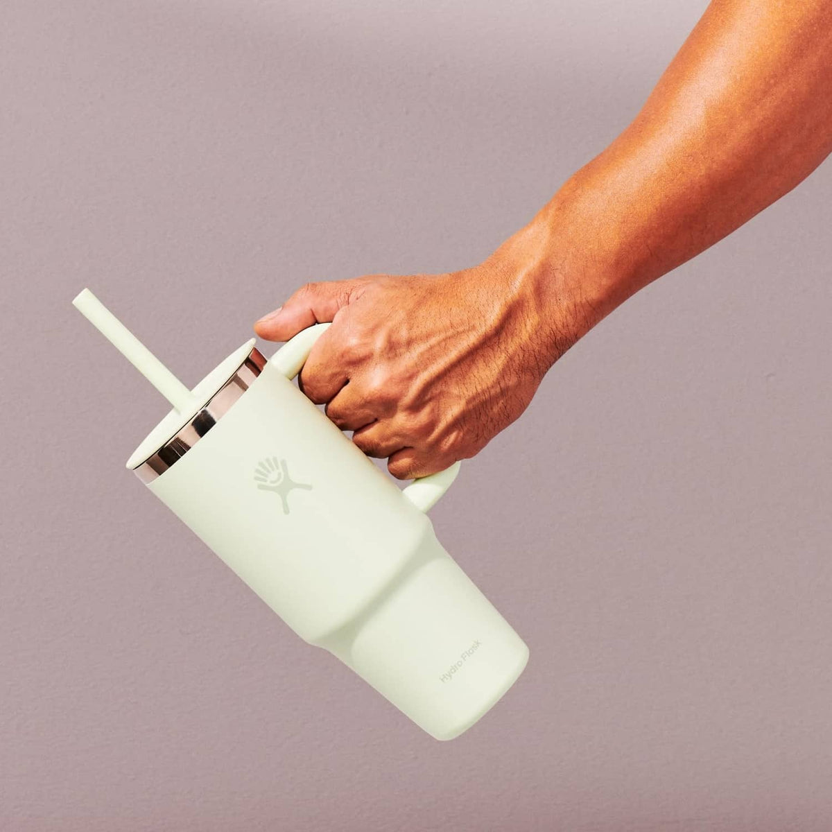 Sage travel tumbler with handle, straw, and lid, held at an angle by hand.
