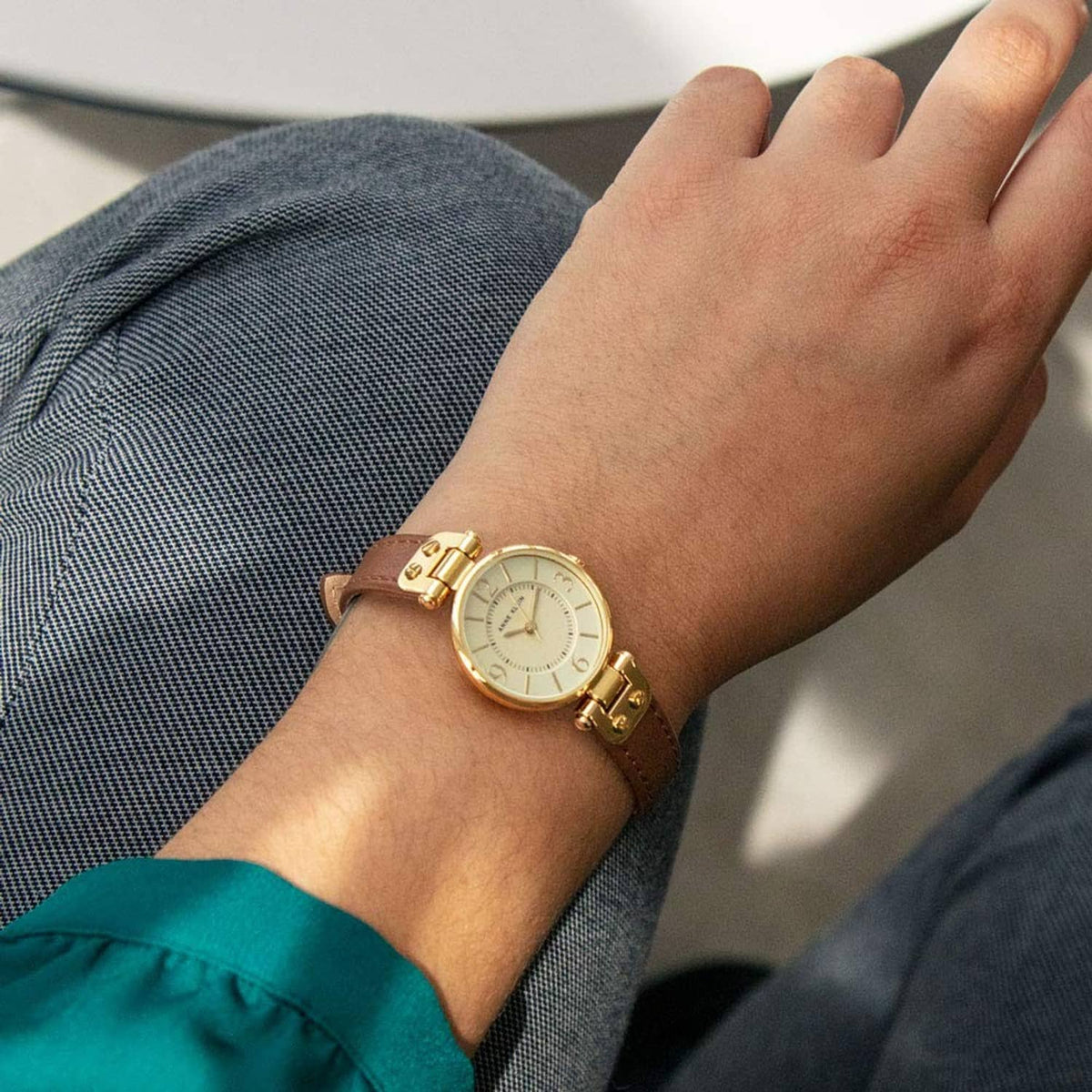 Gold-tone round dial watch on wrist with brown leather strap and linked bezel