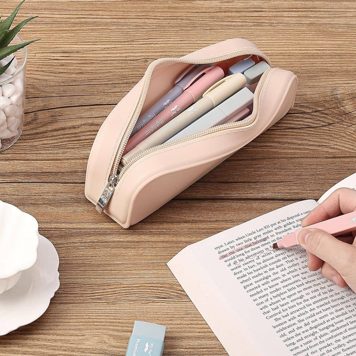 Beige pencil case with zipper open, holding pens on a desk