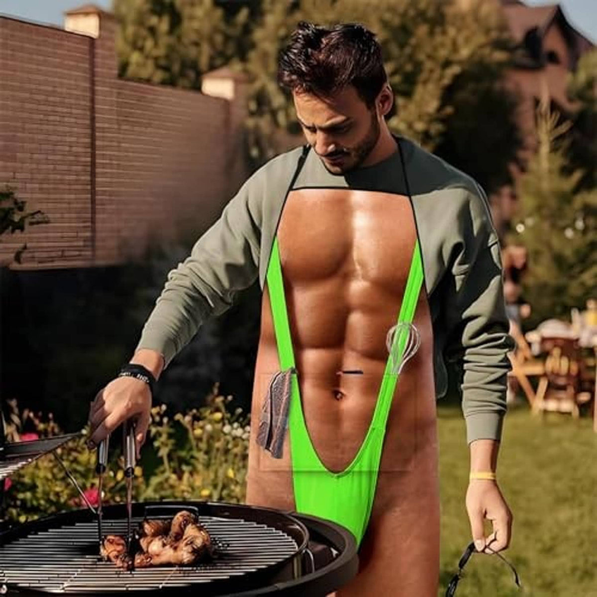 Novelty grilling apron with green trim and printed front worn outdoors, hands on grill tools