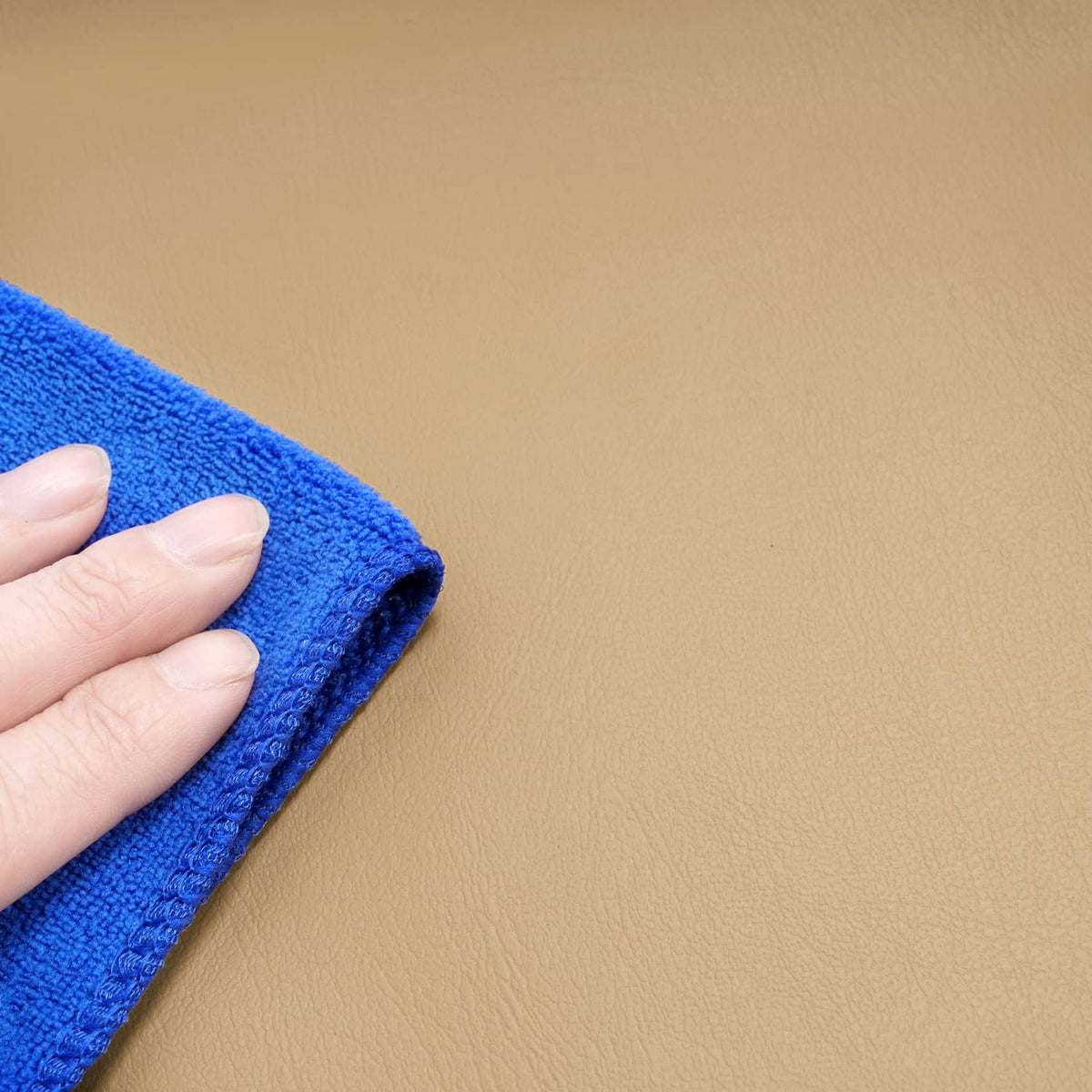 Tan seat back cover surface close-up, hand wiping with blue cloth