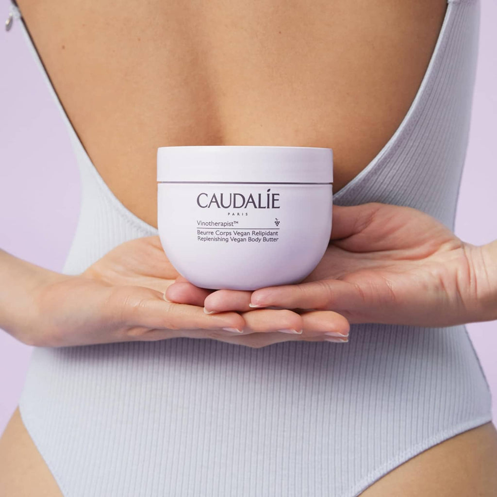 CAUDALIE body butter jar held in hands over a light blue ribbed top