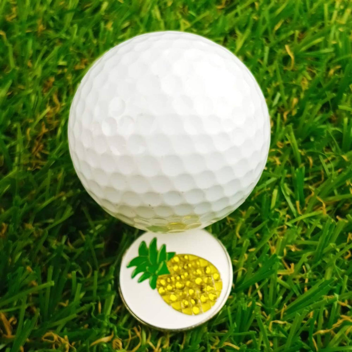 Pineapple golf ball marker coin with silver rim, placed on green grass