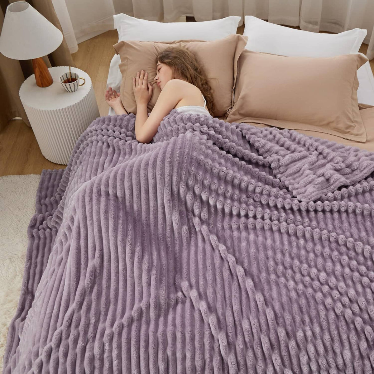 Lavender chunky ribbed fleece blanket covering a bed, with reader and open book