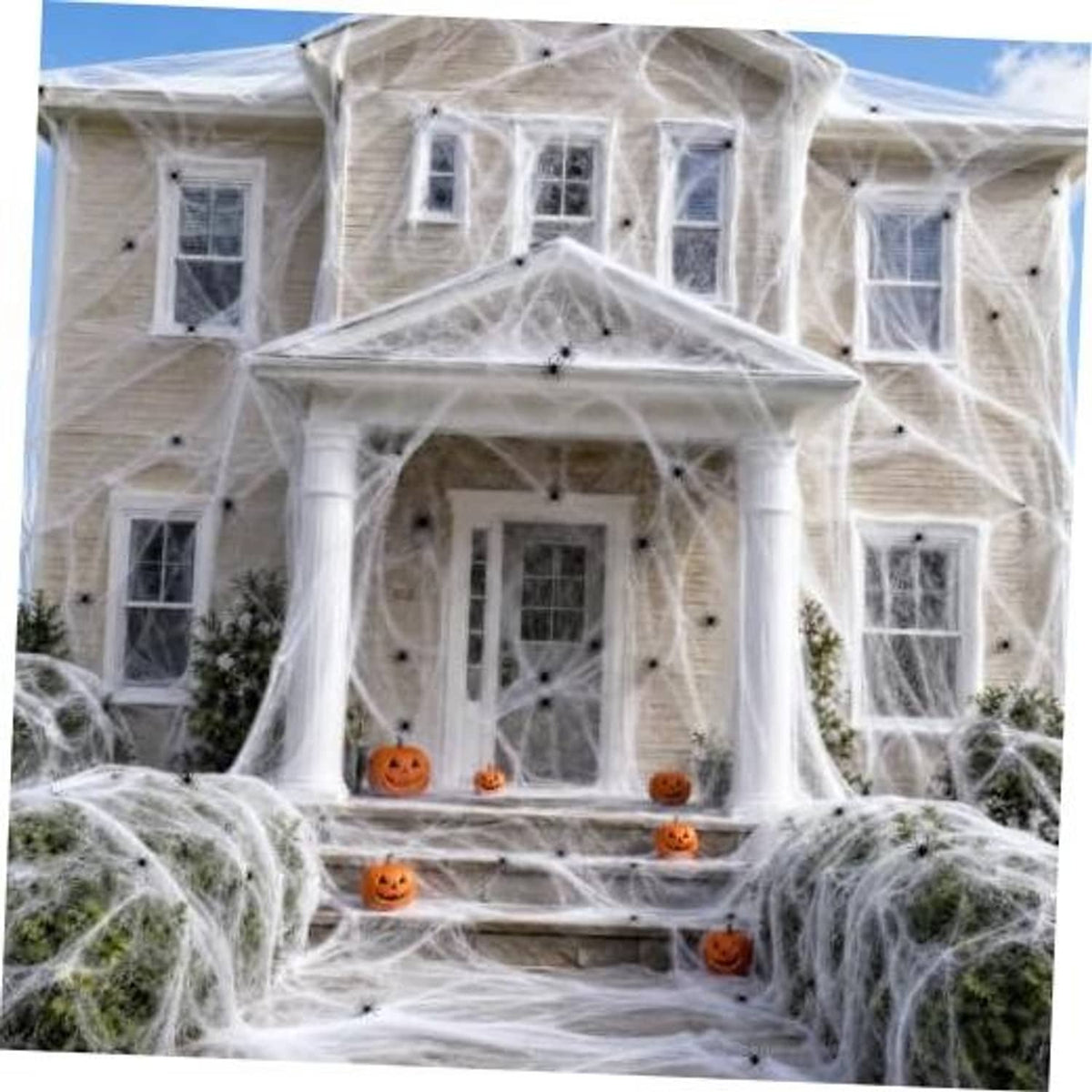 White fabric spider webbing draped over a house facade with orange jack-o-lanterns