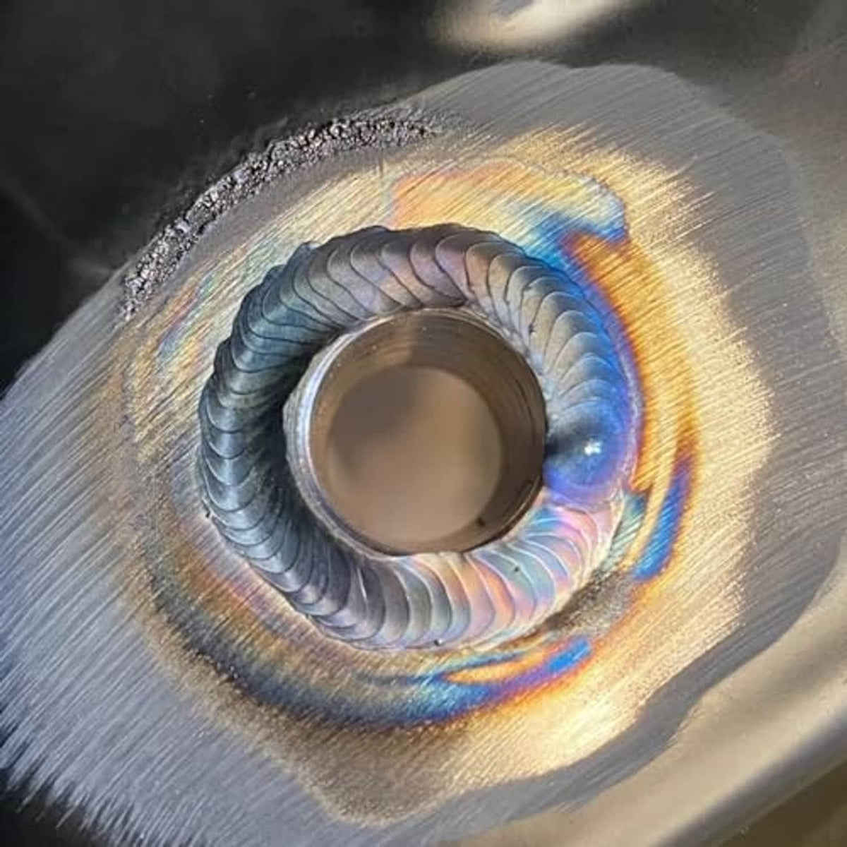 Welded male bung fitting on metal surface, showing rainbow heat tint around threads