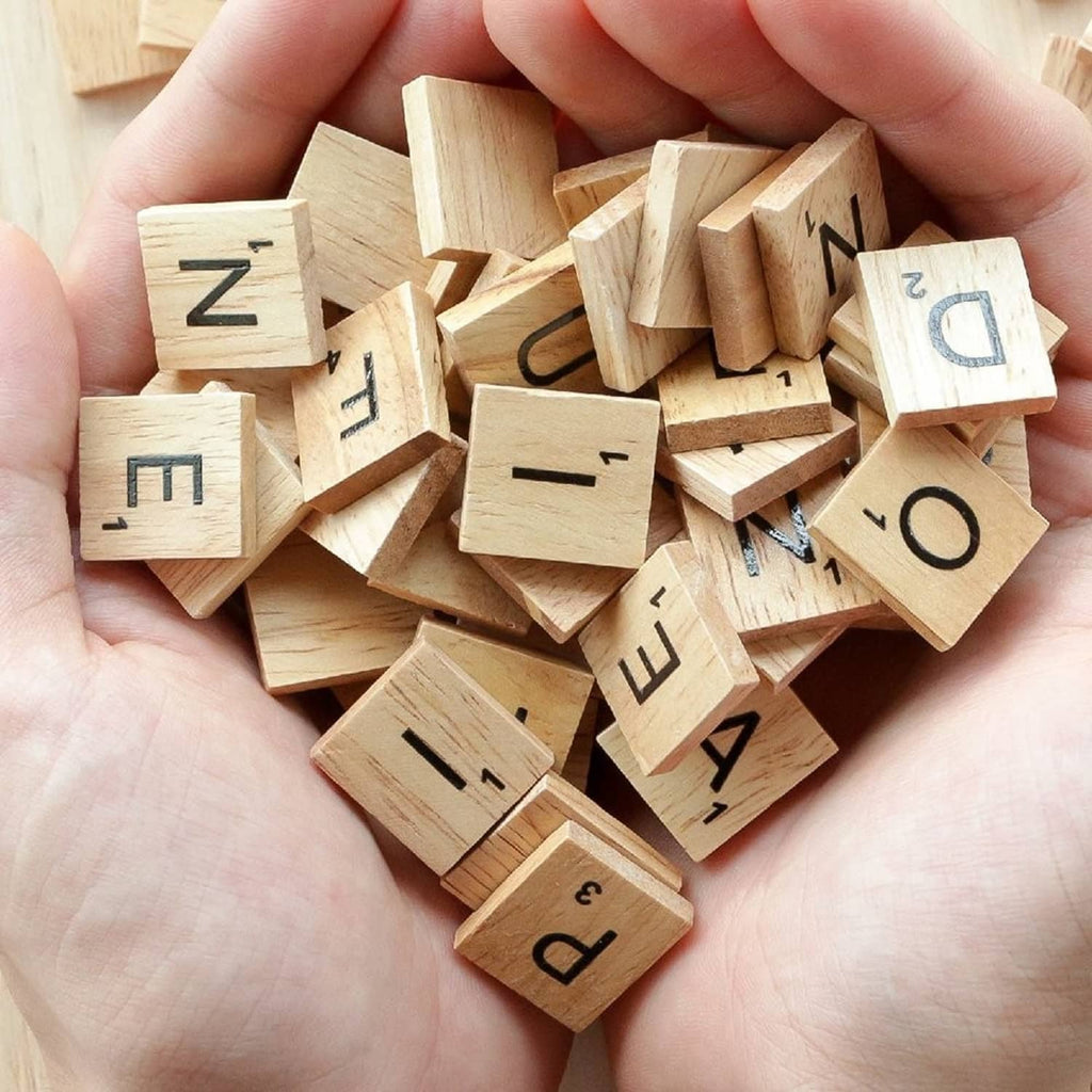 Handful of QMET wood letter tiles with dark printed letters, natural light woodgrain
