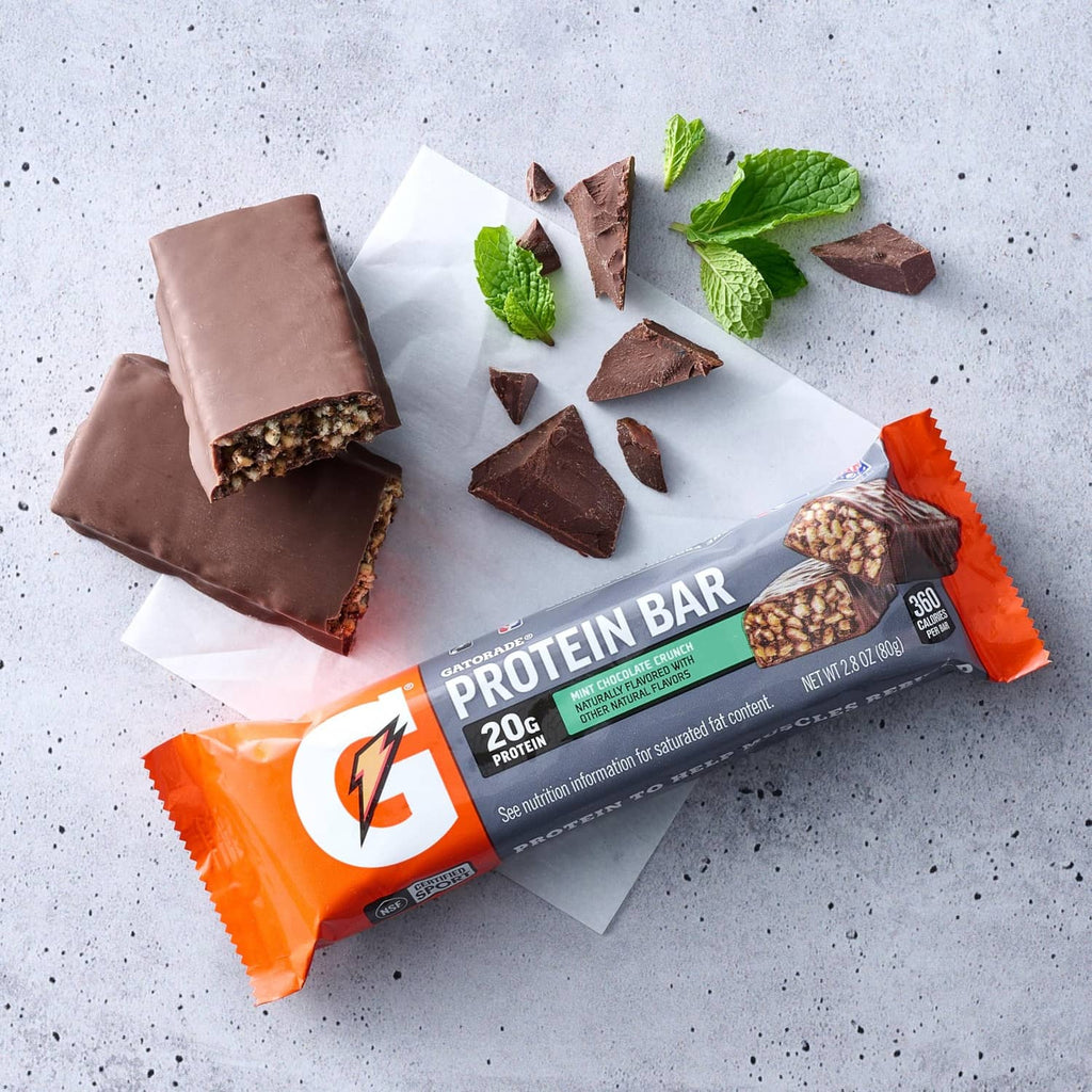Mint chocolate crunch protein bar pieces with mint leaves on white paper