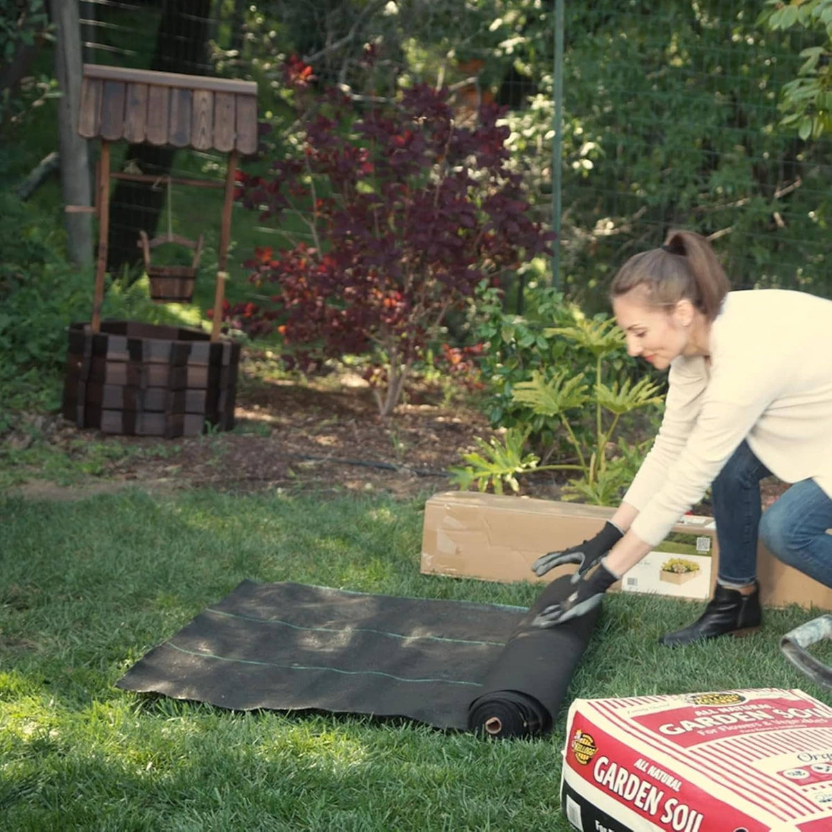 Person laying black landscape weed barrier on lawn, trimming and securing the fabric.