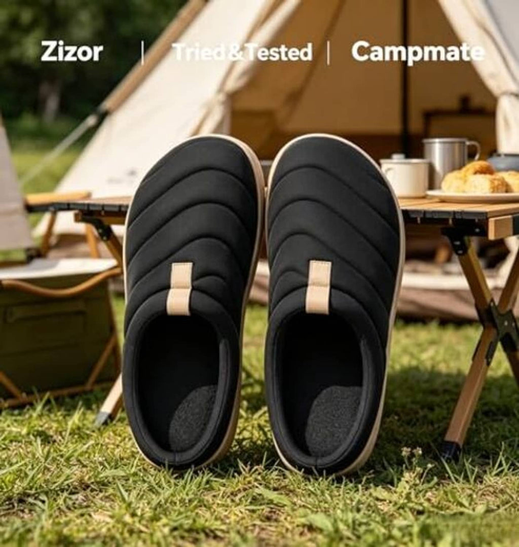 Pair of black quilted slip-on slippers with beige side strap, on grass
