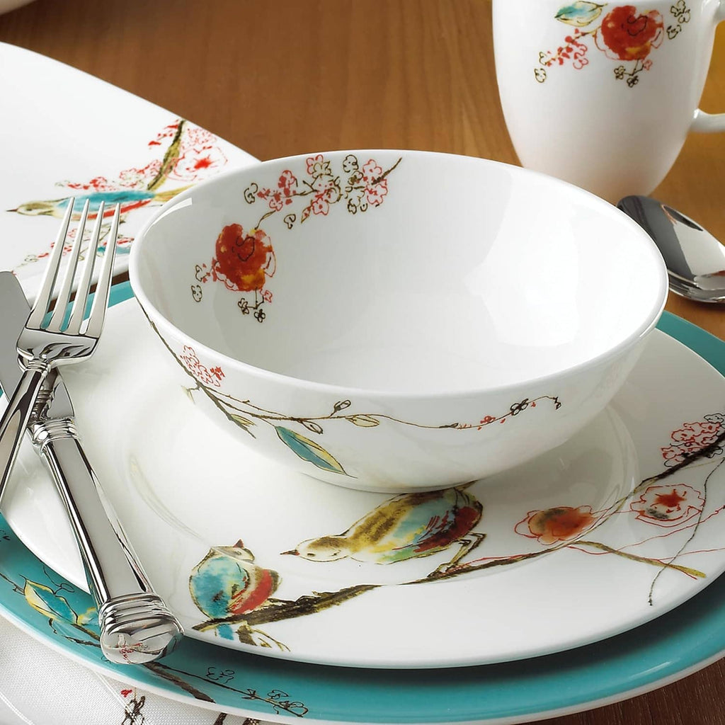 White ceramic bowl with bird-and-floral pattern on teal plate, with fork and knife