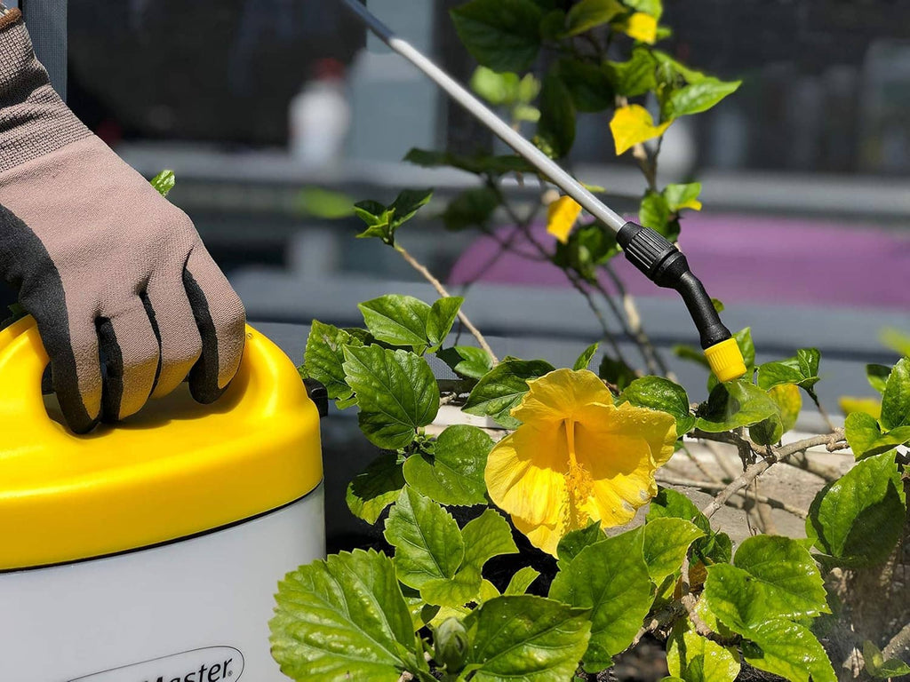 Yellow-and-white battery sprayer nozzle dispensing onto green leaves