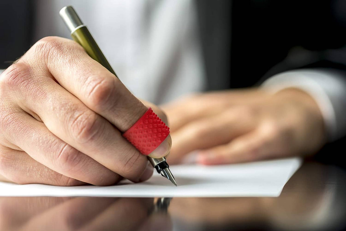 Red finger tip grip ring on a finger writing with a pen