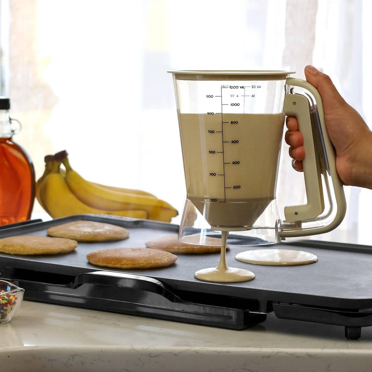 Beige 5-cup batter dispenser pouring batter onto hot griddle
