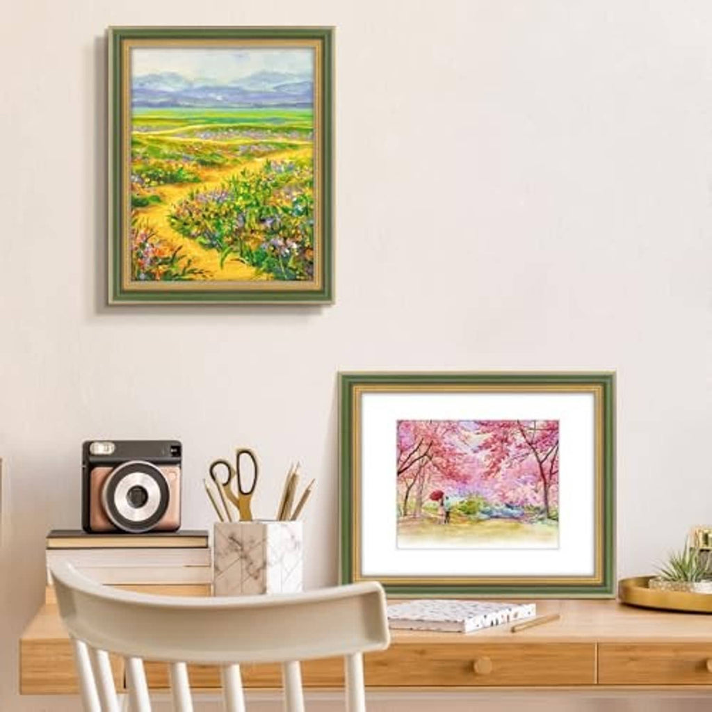 Ornate green and gold picture frames on a desk, displaying landscape and floral artwork.