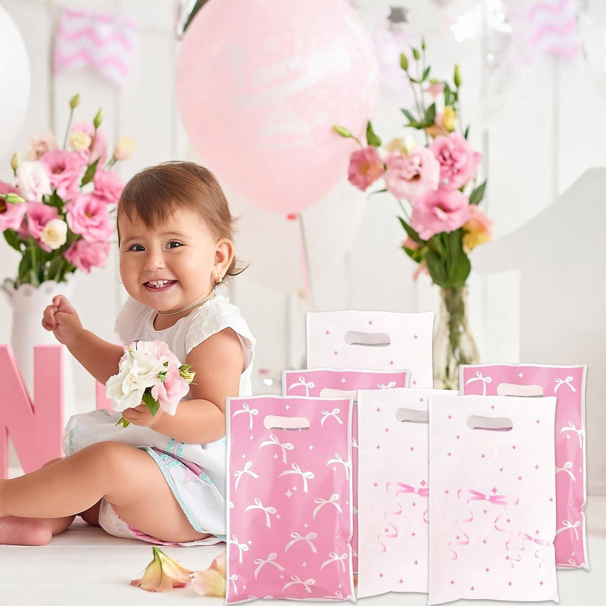 Baby sitting next to pink and white bow-pattern gift bags with handle cutouts