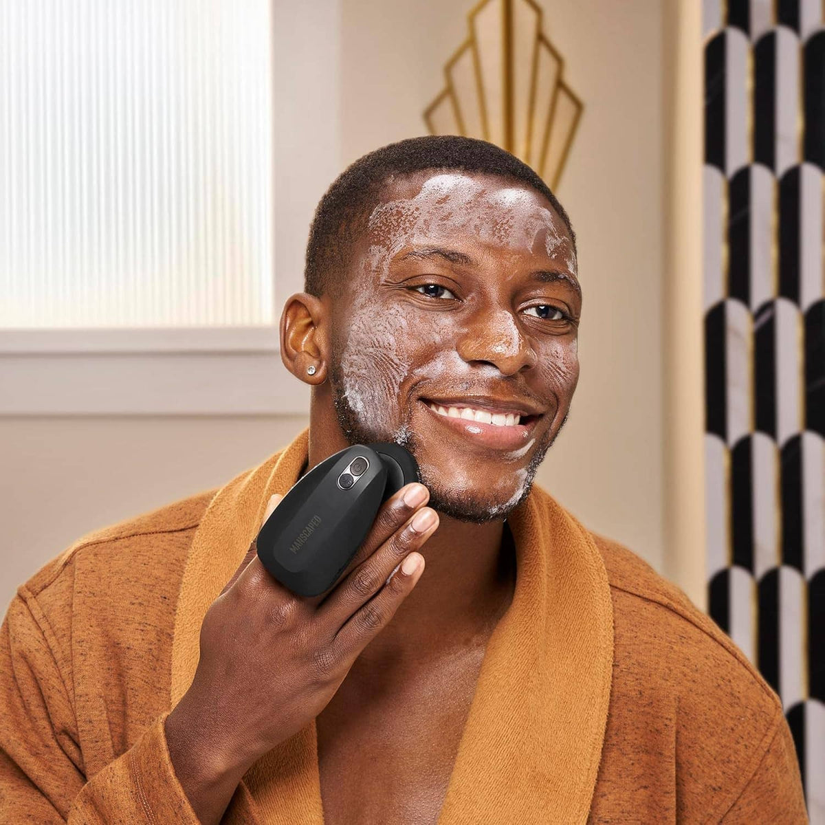Smiling man holding electric silicone face scrubber near his beard area