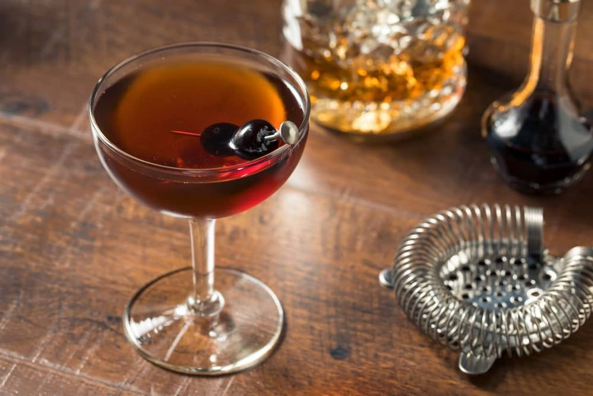 Wine cocktail in a glass with dark maraschino cherry garnish on wooden table