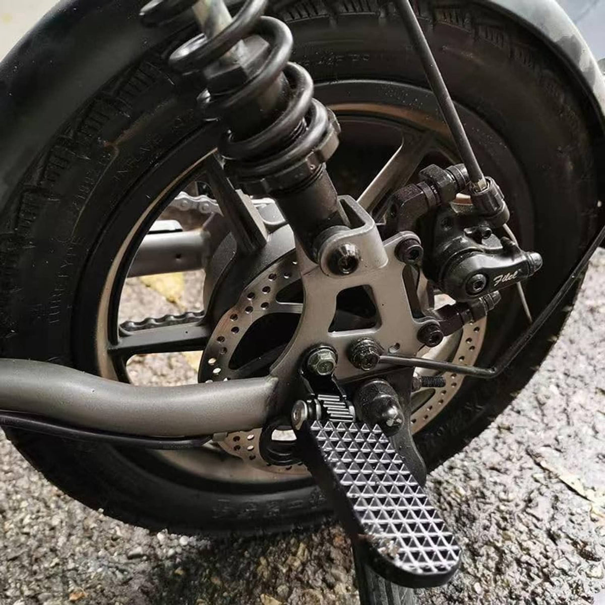 Mounted black textured footpeg on scooter near front brake and wheel