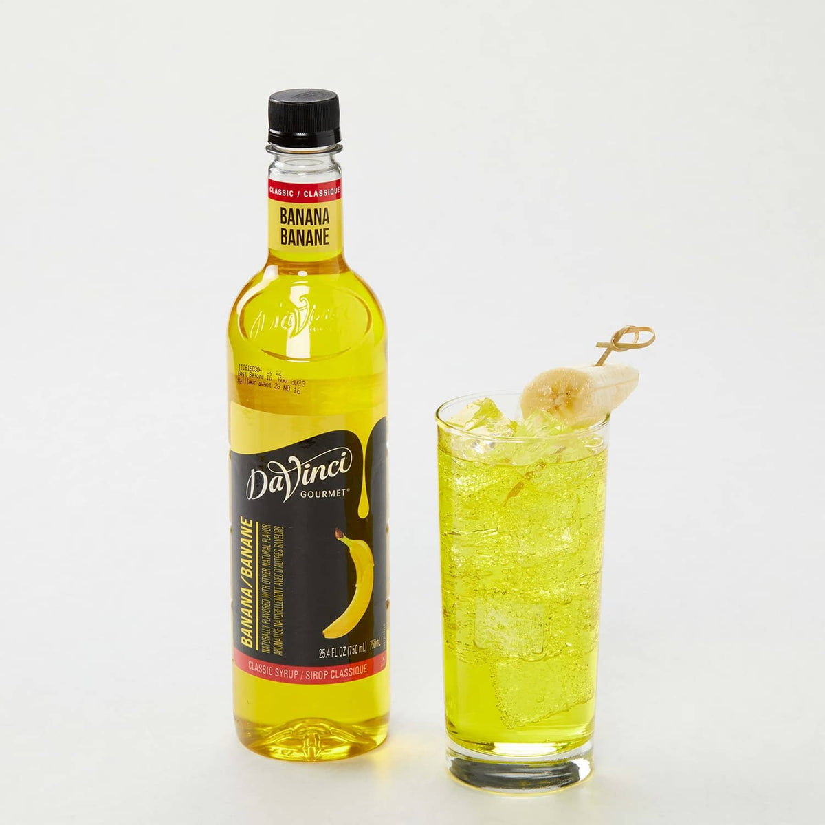 Banana syrup bottle with tall glass of yellow drink and ice