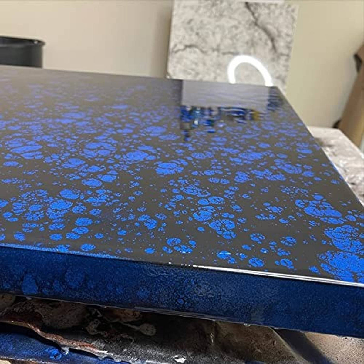 Black epoxy undercoat with blue speckled bubbles on a glossy tabletop
